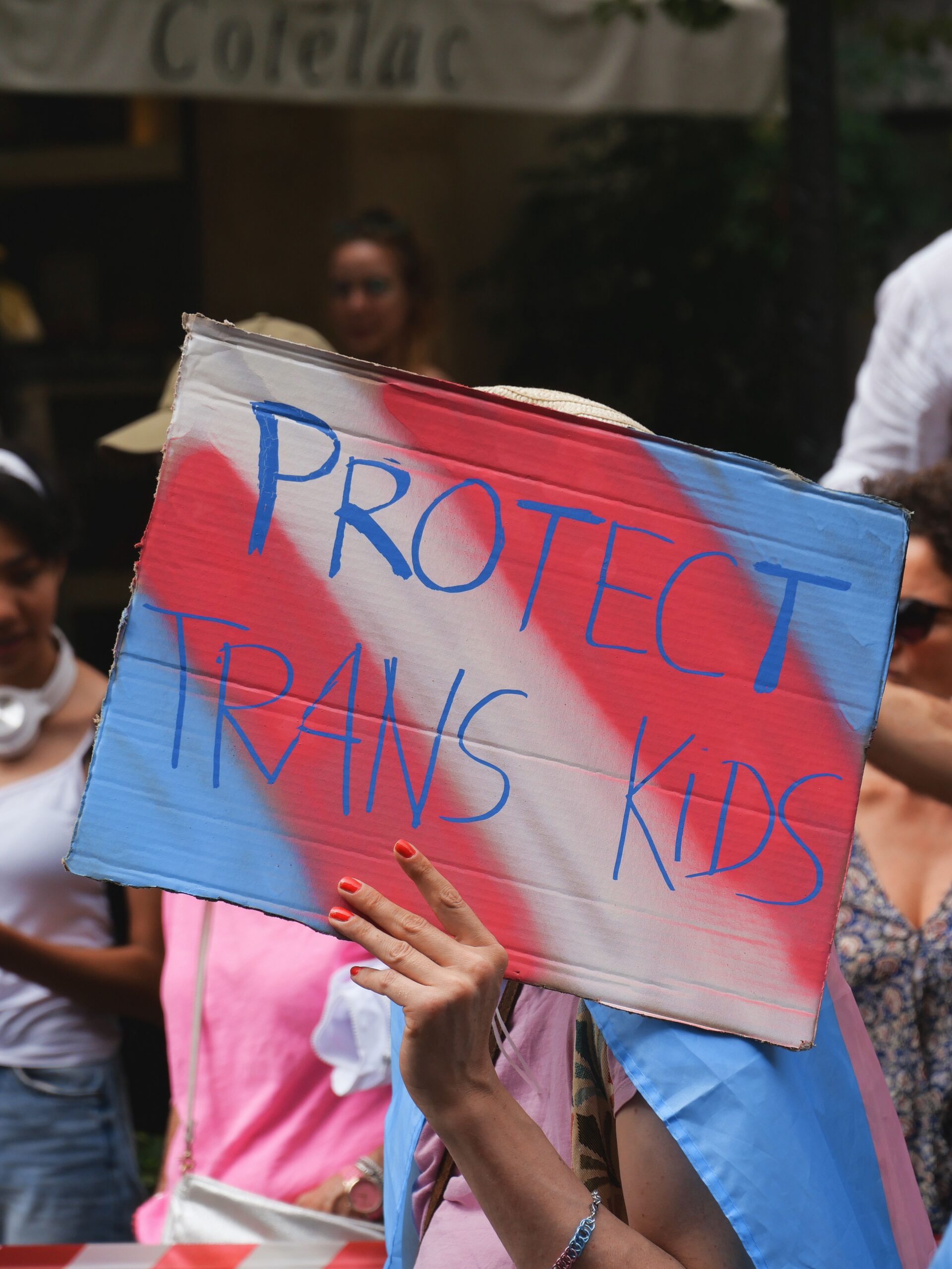A hand-painted sign reading 'Protect trans kids' held up at a march